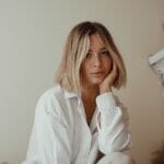 A woman in a white shirt leaning against a wall.