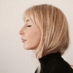 A woman with blond hair in a black turtleneck.