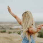 A woman standing on a hill with her arms outstretched.