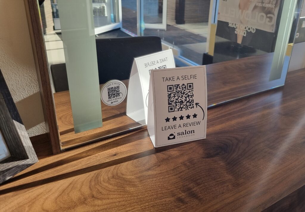 A mirror displaying a sign with a QR code for client selfies and reviews.