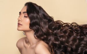 A woman with long curly hair is posing on a yellow background.