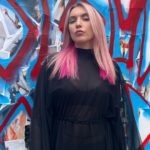 A woman with pink hair standing in front of a graffiti wall.