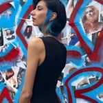 A woman in a black dress standing in front of a wall covered in graffiti.