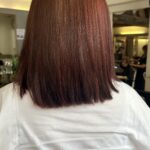 A person with straight, shoulder-length reddish brown hair is shown from behind, wearing a white top, in the chic Heaven Hair Salisbury salon with mirrors and chairs visible.
