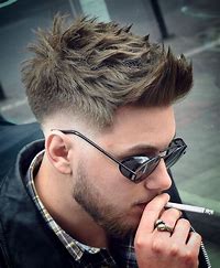 A man with styled spiked hair, sunglasses, and a beard, wearing a plaid shirt and leather jacket, holds a cigarette near his mouth.
