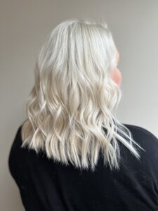 Person with shoulder-length, wavy platinum blonde hair, seen from behind, wearing a black top against a plain background.